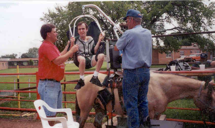 Two staff members using adaptive saddle lift to lift client onto a horse.
